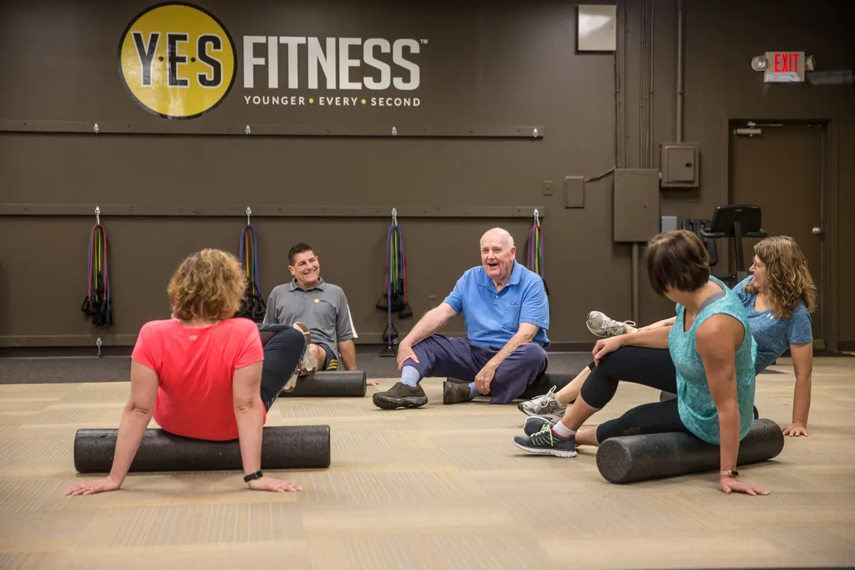 YES Fitness members and a coach laughing together during a group foam rolling session