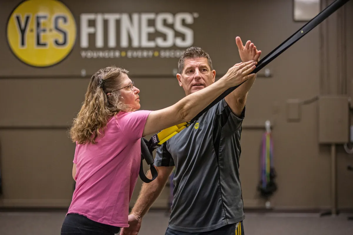 A YES Fitness coach correcting a member's arm position during a TRX single-arm row