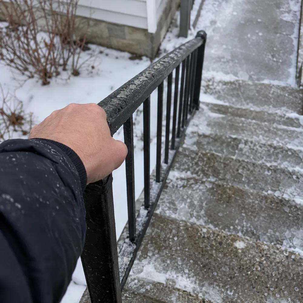 A hand gripping an icy black railing on snowy outdoor steps