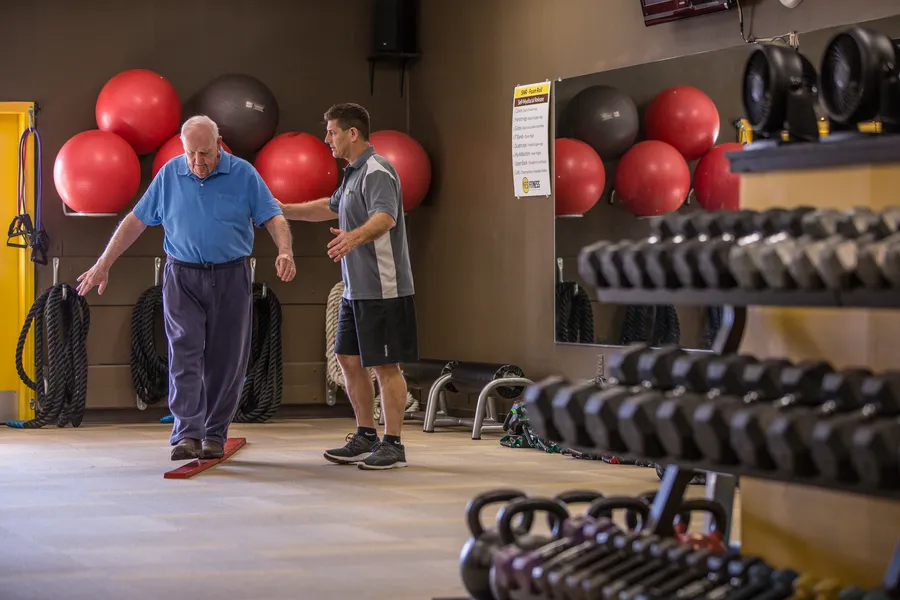 Peter walking heel to toe along a red balance board with his coach beside him at YES Fitness