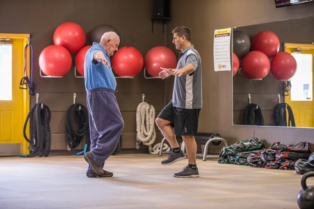 Peter balancing on one leg while his coach guides him at YES Fitness